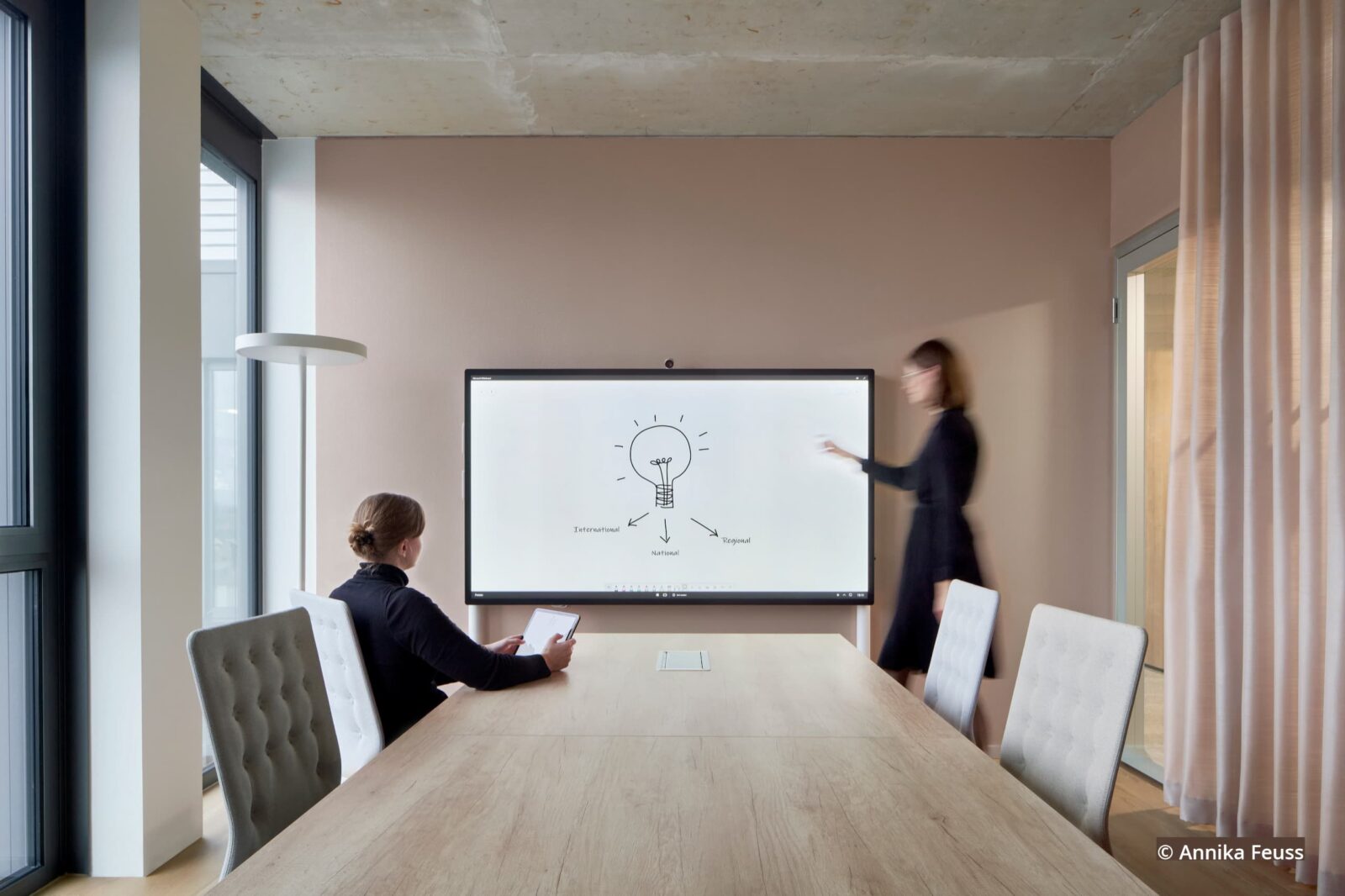 Besprechungsraum mit digitalem Whiteboard in dem zwei Personen arbeiten