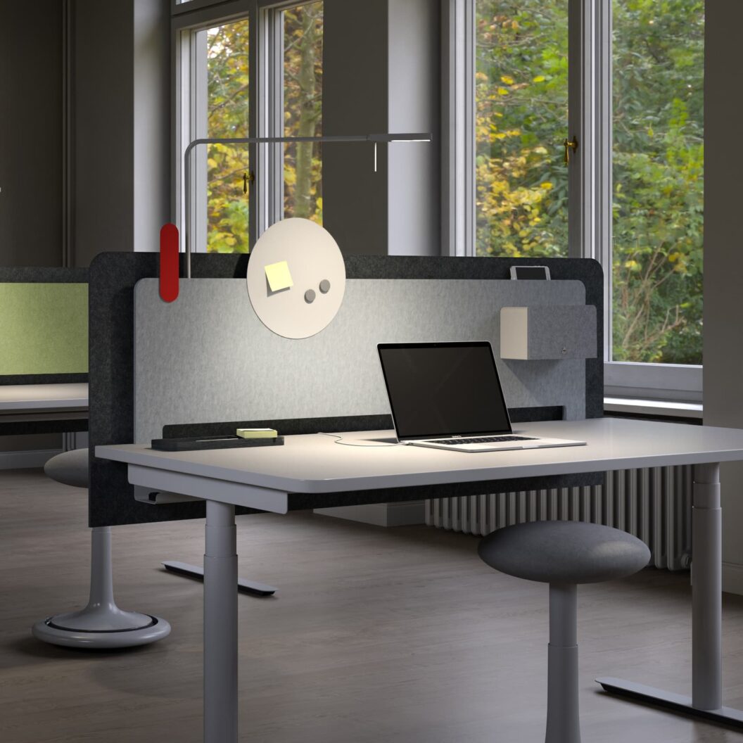 Bildausschnitt mit einem Arbeitsplatz mit Akustikwand in die eine Leuchte integriert ist, ein Magnetboard und ein abschließbarer Safe