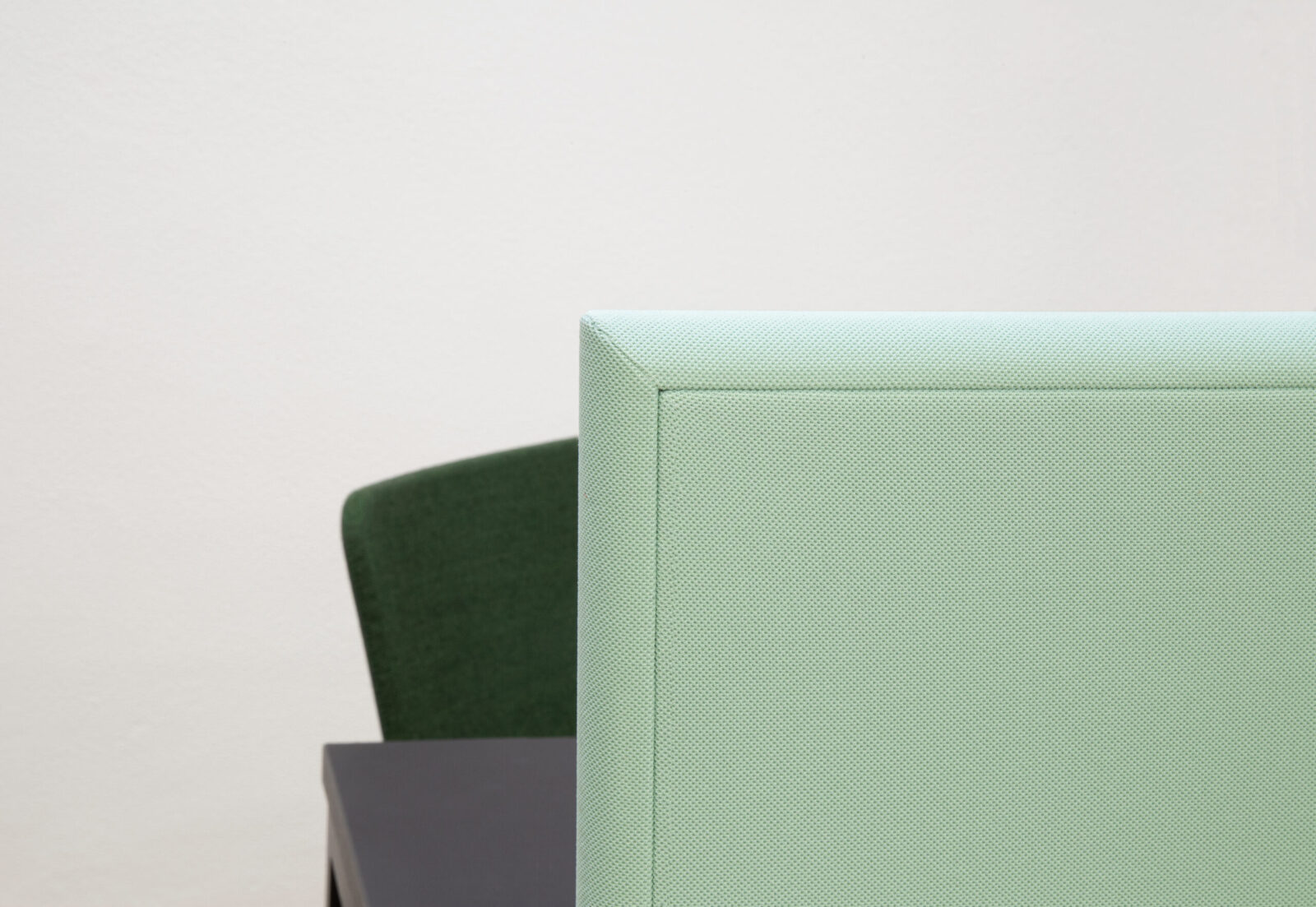 Bildausschnitt zeigt einen Teil einer textilumspannten Tischaufsatzwand. Der Stoff ist hellgrün. Dahinter steht ein schwarzer Tisch mit grünem Stuhl.